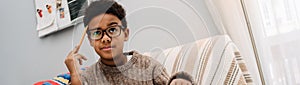 Black puzzled boy doing homework while sitting on sofa