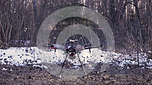 Black quadcopter taking off from the ground in the forest with many leaves flying into the sides. Clip. A drone starting