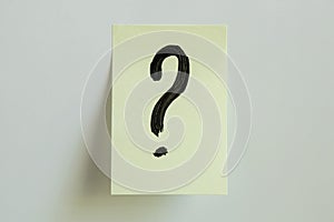 A black question mark painted on a yellow sticky note placed on a white