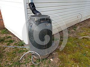 Black rain barrel with gutter downspout and hose
