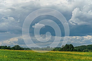 A black rain cloud over a rural field. The rays of the setting sun are breaking through a terrible gray cloud. On the eve of the