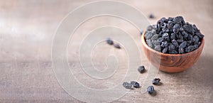 Black raisins in wooden bowl on wood textured background. Copy space. Superfood, vegan, vegetarian food concept. Macro of fresh