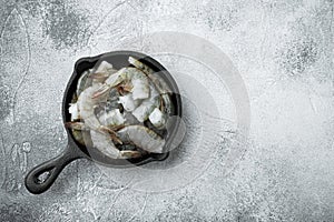 Black raw tiger shrimps, in cast iron frying pan, on gray stone background, top view flat lay, with copy space for text