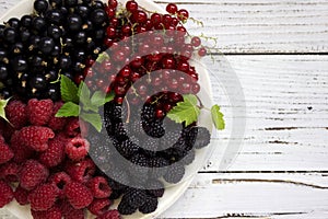 Black and red currants, black and red raspberries on a plate with a leaf of raspberry, white background