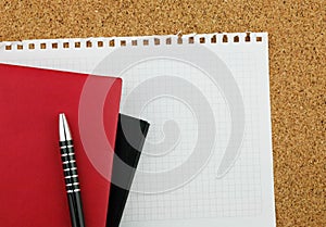 Black and red notebooks on the clean white sheet with black pen on the cork board background.