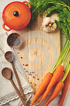 Black and red pepper, basil leaves, carrots, ceramic pan, wooden stand, simple old spoons and linen napkin on light background.