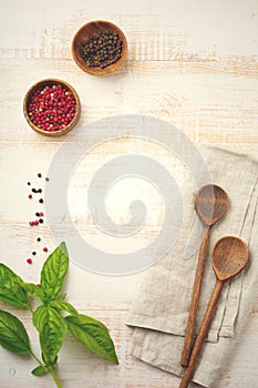 Black and red pepper, basil leaves, carrots, ceramic pan, wooden stand, simple old spoons and linen napkin on light background.