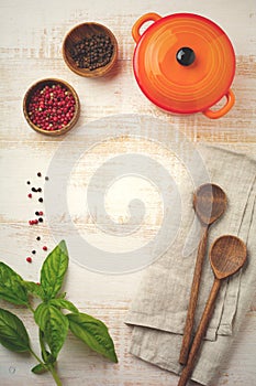 Black and red pepper, basil leaves, carrots, ceramic pan, wooden stand, simple old spoons and linen napkin on light background.