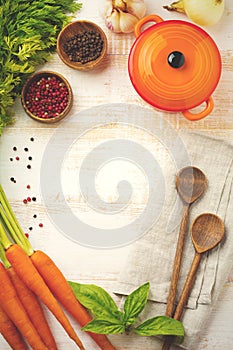 Black and red pepper, basil leaves, carrots, ceramic pan, wooden stand, simple old spoons and linen napkin on light background.