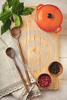 Black and red pepper, basil leaves, ceramic pan, wooden stand, simple old spoons and linen napkin on light background. Kitchen