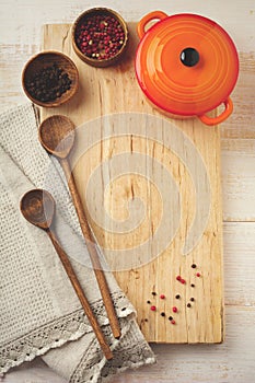 Black and red pepper, basil leaves, ceramic pan, wooden stand, simple old spoons and linen napkin on light background. Kitchen