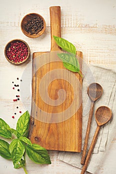 Black and red pepper, basil leaves, ceramic pan, wooden stand, simple old spoons and linen napkin on light background. Kitchen