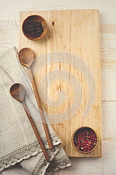 Black and red pepper, wooden stand, simple old spoons and linen napkin on light background. Kitchen accessories concept. Selective