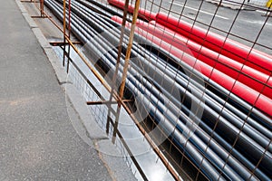 Black and red PVC pipes for underground cables and structures at a construction site on a city street.