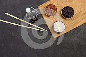 Black, red and white rice in wooden bowls. Soy sauce in glass jar. Bamboo sticks