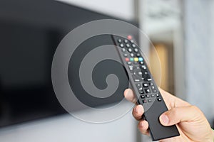 Black remote control in hand in front of TV