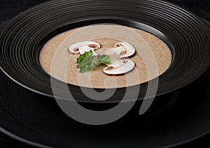 Black restaurant plate of creamy chestnut champignon mushroom soup on black table background