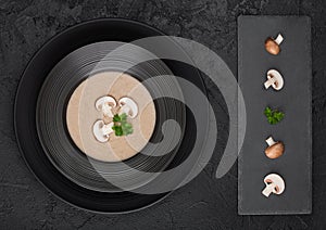 Black restaurant plate of creamy chestnut champignon mushroom soup on black table background with black stone board and fresh