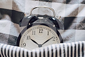 Black retro alarm clock sleeping on pillow with blanket metaphor of insomnia, late at work, well sleep with time countdown or wake