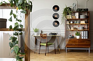 Black retro typewriter on a unique wooden desk, a mid-century modern chair and a renovated bookcase in a hipster home office inter