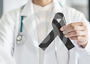 Black ribbon awareness in doctor`s hand for Melanoma and skin cancer, Narcolepsy, Primary Biliary Cirrhosis Cholangitis