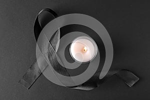 Black ribbon and burning candle on dark background. Funeral symbols