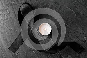 Black ribbon and burning candle on dark  stone surface, top view. Funeral symbols