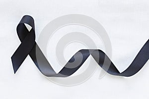 Black ribbon curl on white fabric background with copy space, symbol of Skin Cancer awareness month on May, Melanoma cancer,