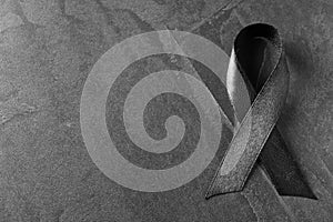 Black ribbon on dark grey stone surface, topwith space for text. Funeral symbol