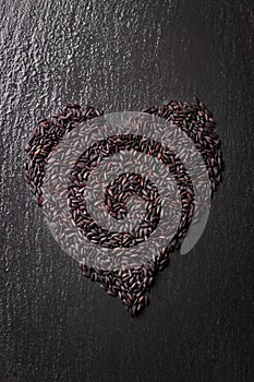 Black rice in heart shape on a black stone background with water droplets