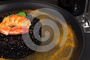 Black rice risotto with shrimp and safron in a black plate in dark background close photo