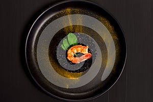 Black rice risotto with shrimp and safron in a black plate seen from above in dark background