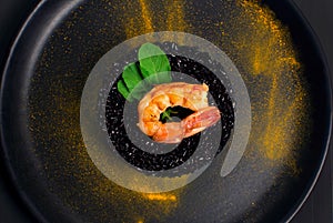 Black rice risotto with Shrimp and safron in a black plate seen from above in dark background close