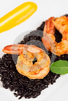 Black rice risotto with shrimp and safron sauce in a white plate seen from above in white background close