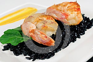 Black rice risotto with shrimp and safron sauce in a white plate seen in white background