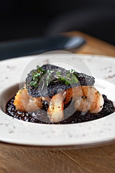 Black rice risotto. Shrimp risotto on a white plate on the table, serving in a restaurant, menu food concept photo