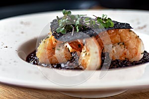Black rice risotto. Shrimp risotto on a white plate on the table, serving in a restaurant, menu food concept photo
