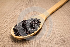 Black Rice seed. Spoon and grains over wooden table.