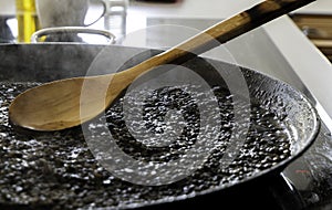 Black rice with squid being cooked in a paella pan and a wooden spoon. Black rice with cuttlefish. Rice al nero di sepia