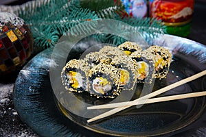 Black rice Sushi roll with Unagi Eel served with chopsticks on Christmas decorated plate