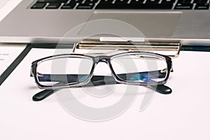 Black rimmed glasses and a computer. Office employee workplace. Tax calculation, report or stock market analysis