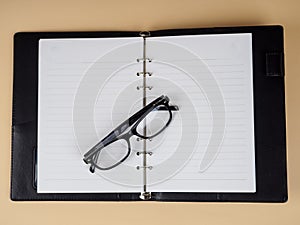 Black-rimmed glasses lie on a book, a notebook