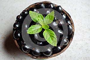 Black ripe Syzygium cumini fruits. Dark black java plum in a wood bowl at isolated white background. Green mint leaf on top of