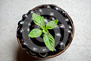 Black ripe Syzygium cumini fruits. Dark black java plum in a wood bowl at isolated white background. Green mint leaf on top of