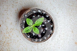 Black ripe Syzygium cumini fruits. Dark black java plum in a wood bowl at isolated white background. Green mint leaf on top of