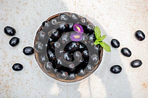 Black ripe Syzygium cumini fruits. Dark black java plum in a wood bowl at isolated white background. Green mint leaf on top of