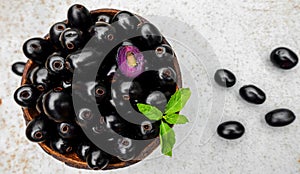 Black ripe Syzygium cumini fruits. Dark black java plum in a wood bowl at isolated white background. Green mint leaf on top of