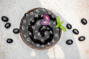 Black ripe Syzygium cumini fruits. Dark black java plum in a wood bowl at isolated white background. Green mint leaf on top of