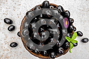Black ripe Syzygium cumini fruits. Dark black java plum in a wood bowl at isolated white background. Green mint leaf on top of