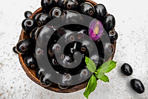 Black ripe Syzygium cumini fruits. Dark black java plum in a wood bowl at isolated white background. Green mint leaf on top of